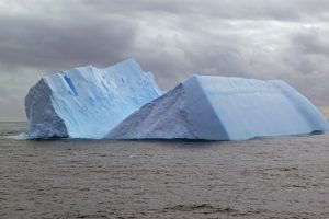 A blue iceberg. split down the middle, against a cloud sky