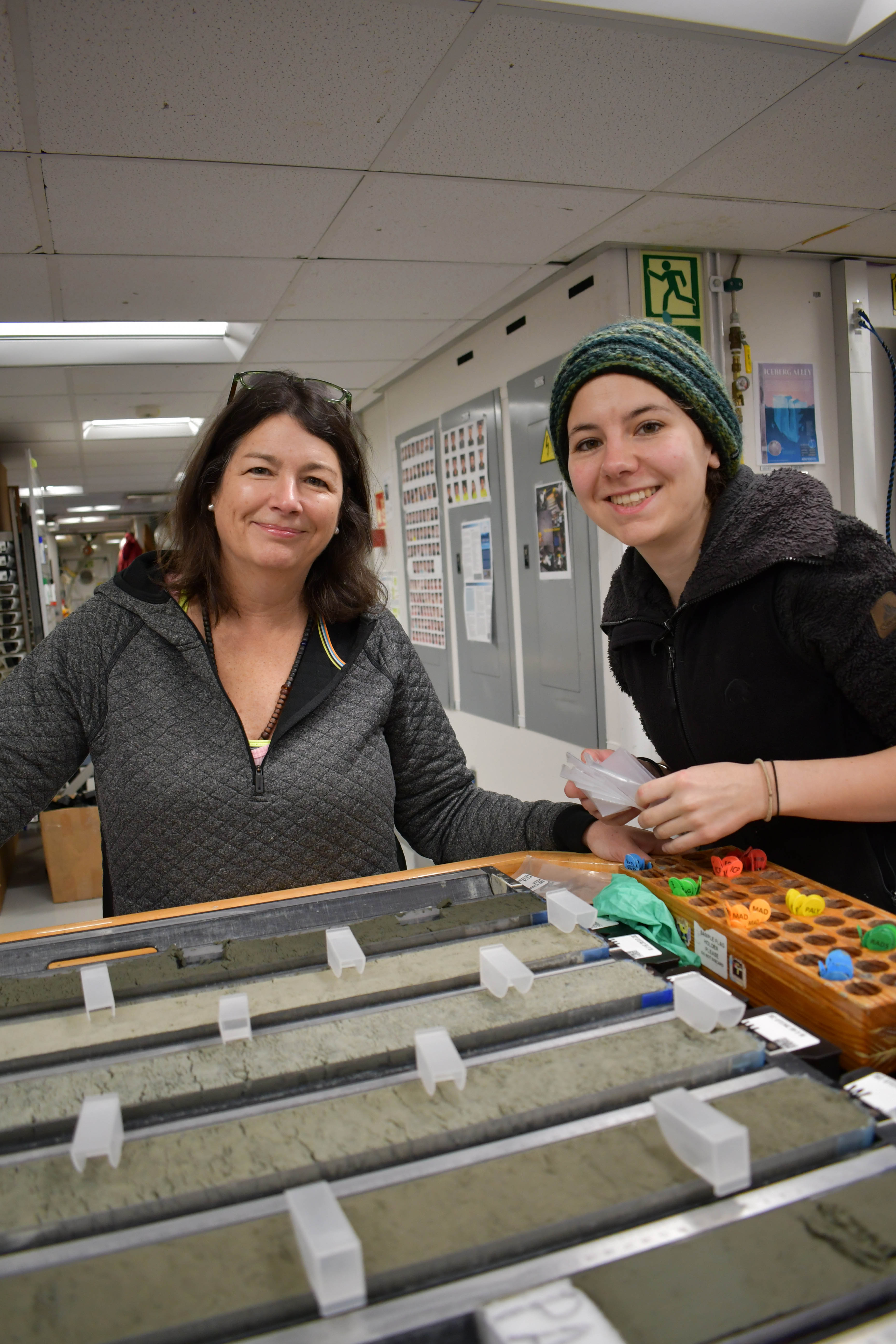 Two smiling women standing at a table filled with sediment cores