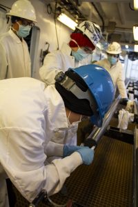 People in hard hats, safety glasses, lab coats, gloves and face masks take samples from a sediment core.