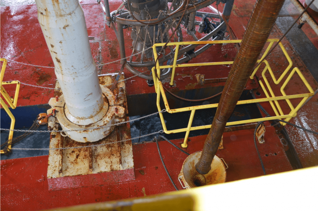 The moon pool of the JR - a vertical slit in the floor of the boat, through which a round pool of ocean water can be seen. A segment of pipe hangs above the moon pool.
