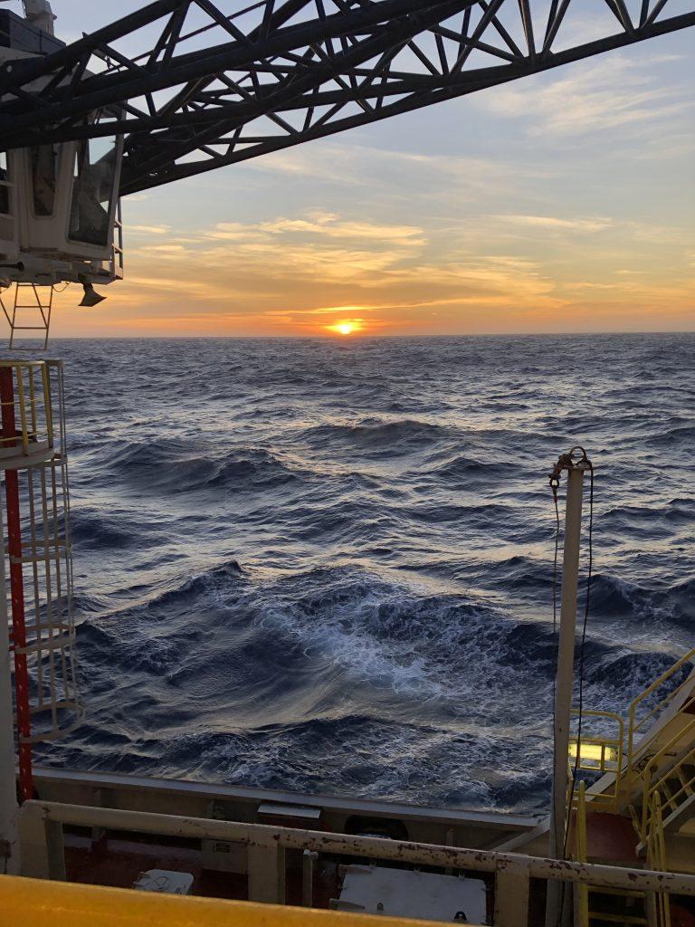A sunrise over rough seas. The arm of a crane stretches over the top of the photo.