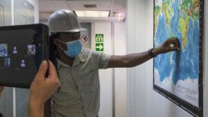 Outreach Officer Maya Pincus holds an iPad while Dr. Mbili Tshiningayamwe points at a map to describe the science of Expedition 391.