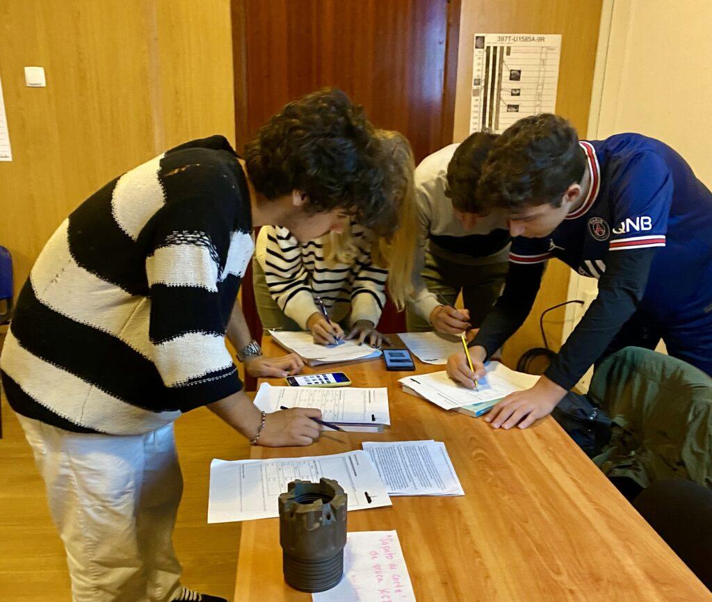 Four Portuguese students lean over a table, working together during an in-school outreach visit.