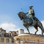 A bronze statue of Dom João I riding a horse with blue sky in the background.