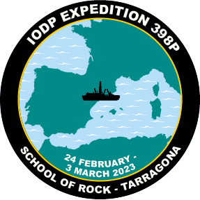 Circular logo with black border. Within boarder is white text. On top "IODPO EXPEDITION 398P" on bottom "SCHOOL OF ROCK - TARRAGONA". Inside border is teal outline of Mediterranean with black silhouette of the JR on the east coast of northern Spain.