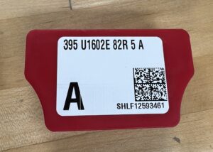 A red plastic cap with a white label reading 395 U1602E 82R 5 A the label also has a QR code on it.