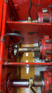 Three long silver metal rods that run from right to left are each in a separate red metal compartment and attached to their own notched red metal wheel on the righthand side