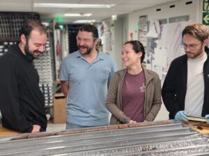 four scientists stand smiling around a core table