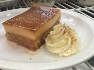 A layered custard dessert with whipped cream on the side. Both sit on a white plate.