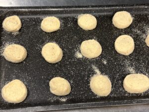 Balls of dough dusted with flour sitting on a dark baking sheet.