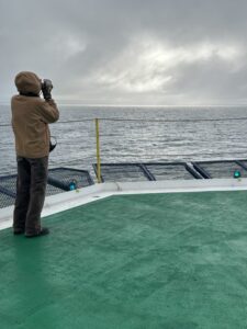 Armed with binoculars and radio, an observer in a brown winter jacket scans the horizon .