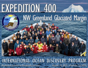 A group of people standing on the bow of a ship. They are dressed for cold weather. A large iceberg is in the background.