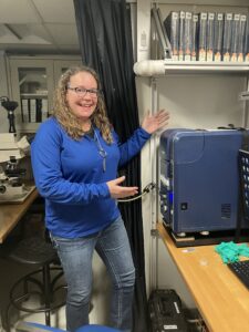 DaNel smiles and points to the scanning electron microscope aboard the JOIDES Resolution.