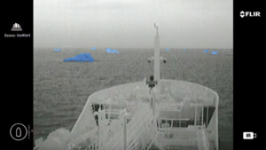 A black and white image of the bow of a ship and the sea beyond. On the water, icebergs show up as blue because of FLIR, thermal imaging binoculars.