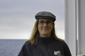 Dr. Sarah Feakins outside on the JOIDES Resolution wearing a gray flatcap.