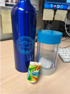 A trimmed core liner and a blue aluminum water bottle displaying an engraved Expedition 401 logo on the front. A shrunken cup sits in front of the two.