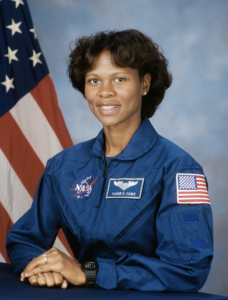 Dr. Yvonne Cagle in her NASA jumpsuit in front of an American flag