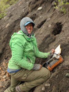 Christina DeVera, wearing a hooded rain jacket, take notes on a soil outcrop.