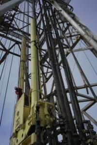 A view of the ship's derrick, a member of the drill crew in the lower lefthand frame. 