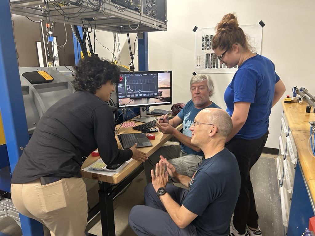 A research team of four are having a discussion around a computer with data outputs.