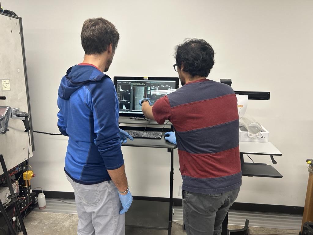 Two men look at data on a computer screen. One man is pointing to the data.